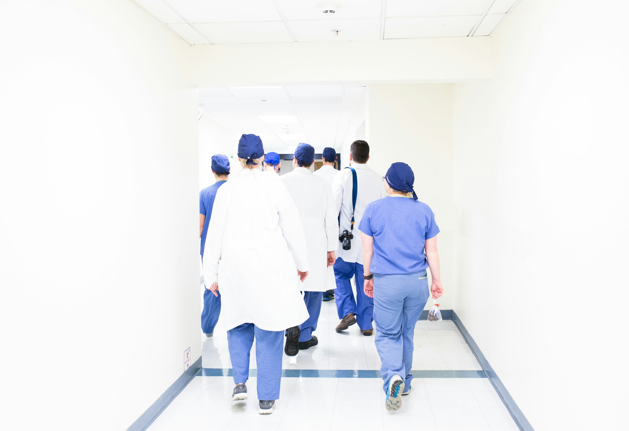A team of healthcare professionals in scrubs and coats walking together down a hospital corridor
